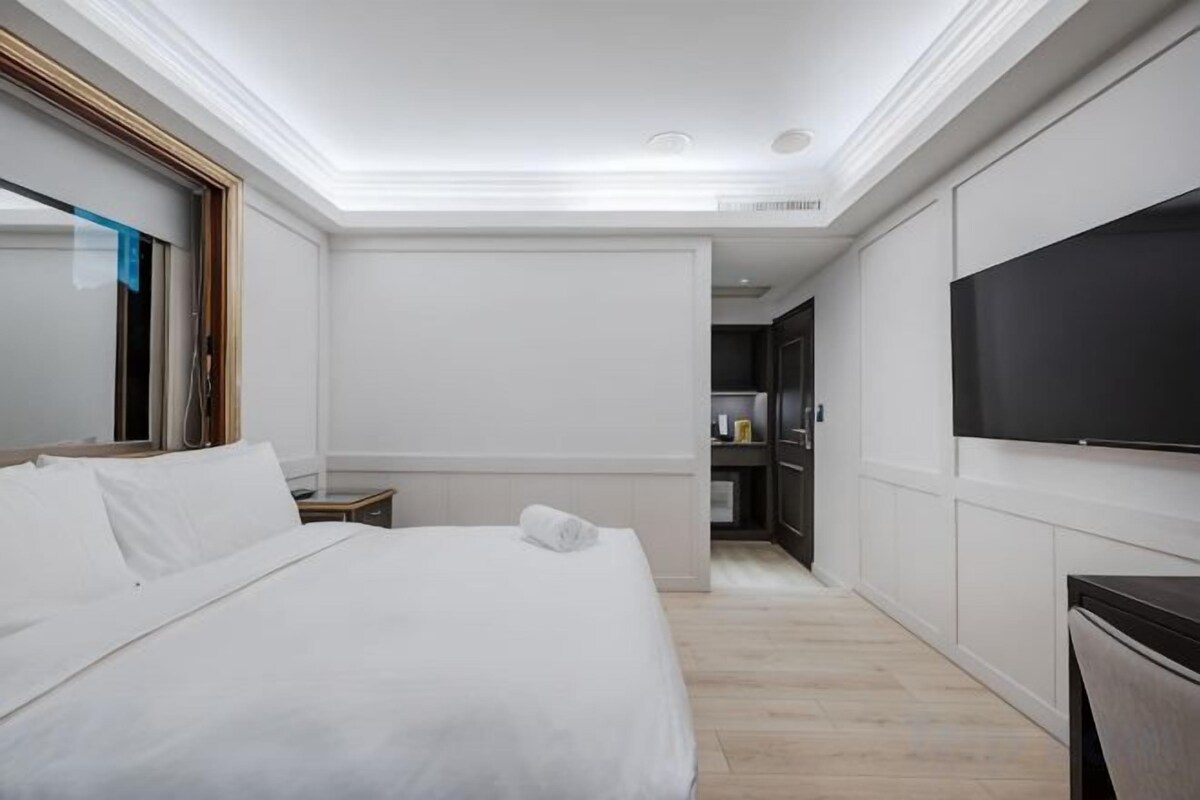 A hotel room with a large bed, a flat-screen TV, a desk, and a wardrobe.