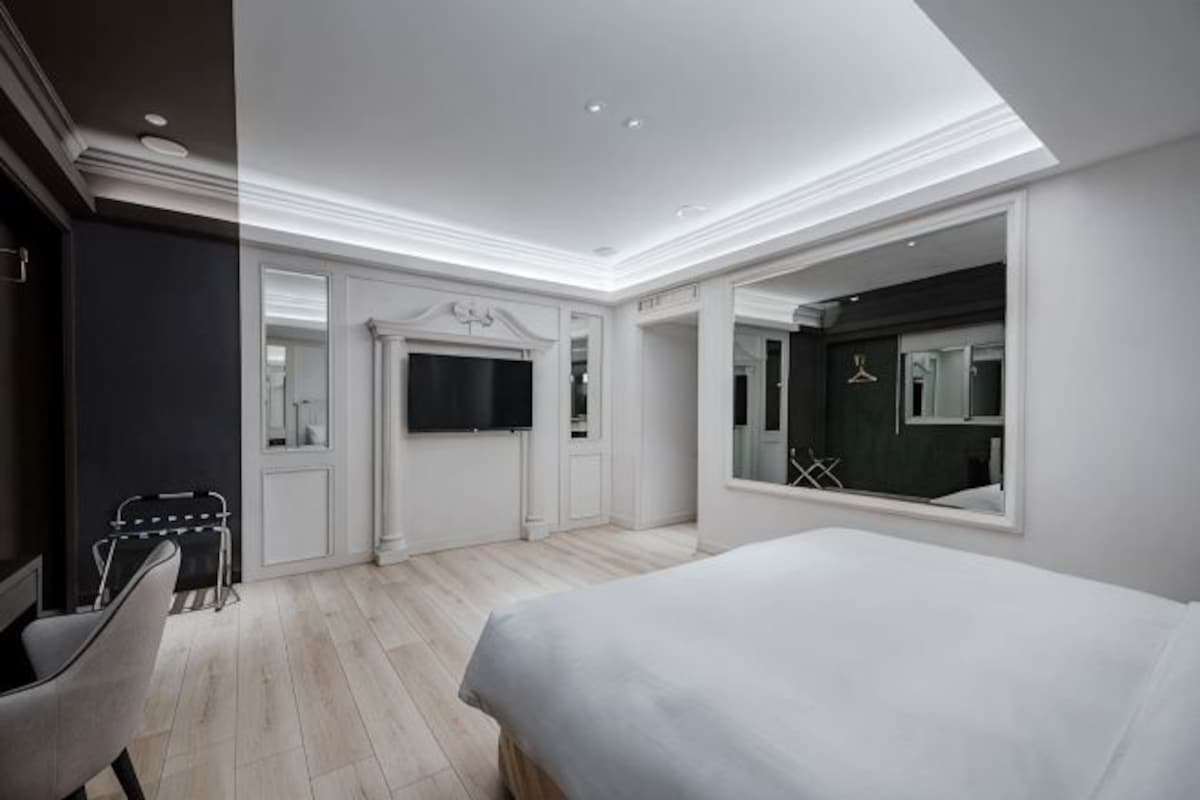 Una habitación de hotel moderna con una cama grande, televisión, espejo y zona de estar.