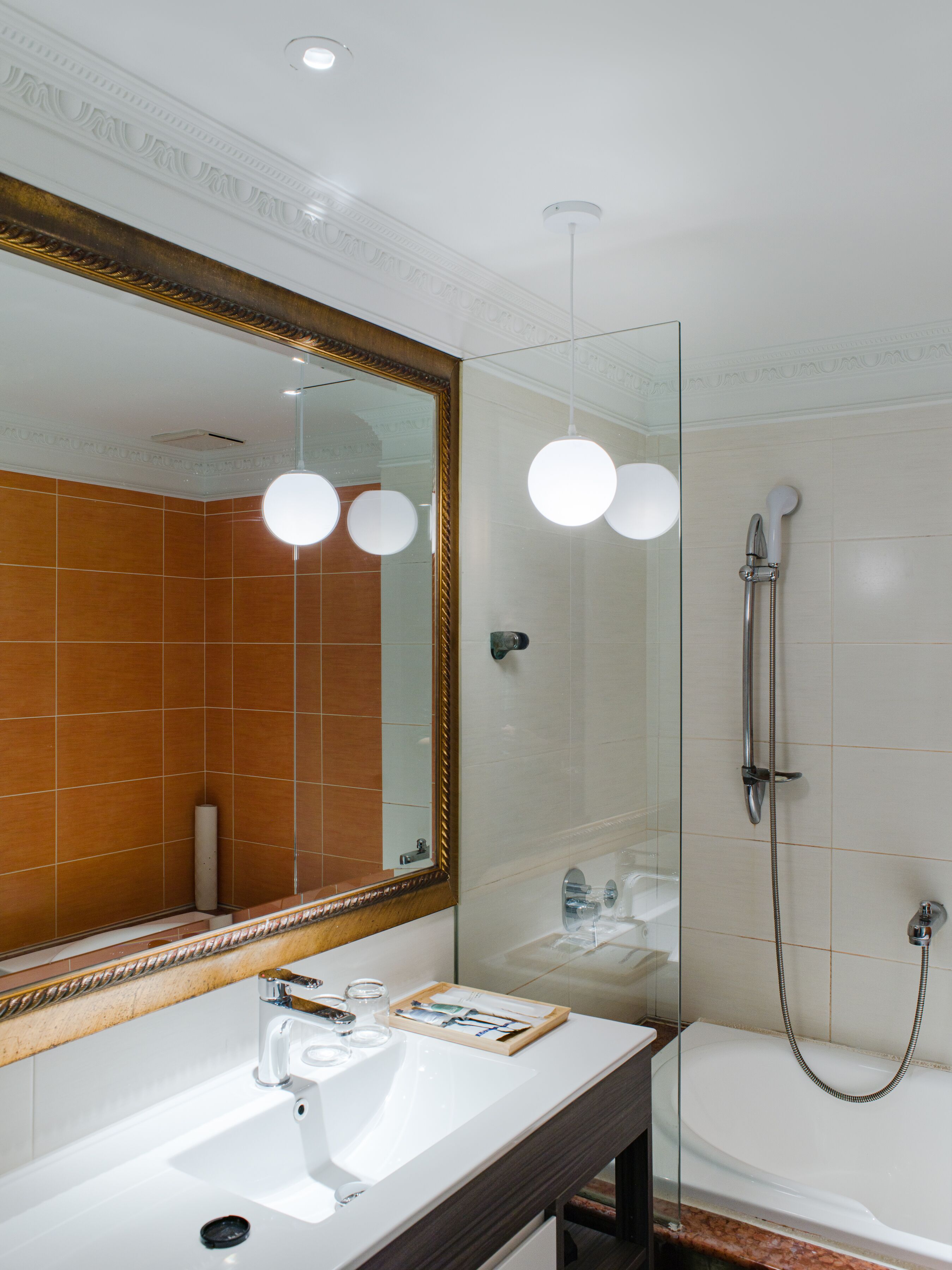 Un baño moderno con un espejo grande, un lavabo blanco, ducha con cerramiento de vidrio y luces colgantes.