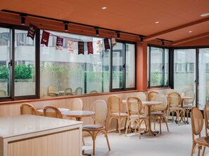 L’intérieur d’un restaurant avec des chaises en osier, des tables rondes et de grandes fenêtres.