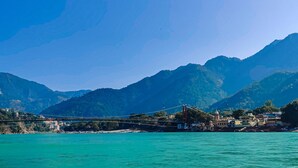 A coastal town with a prominent bridge, mountains in the background, and a clear blue sky. - The Raajas - Camp & Resorts (Yamkeshwar)