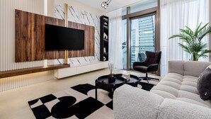 A modern living room with a large flat-screen TV mounted on a wooden panel, a black coffee table, a beige sofa, and a large window with a city view. - Maison Privee - Exclusive Apt w/ Striking Sea & Dubai Marina Vws (Dubai)