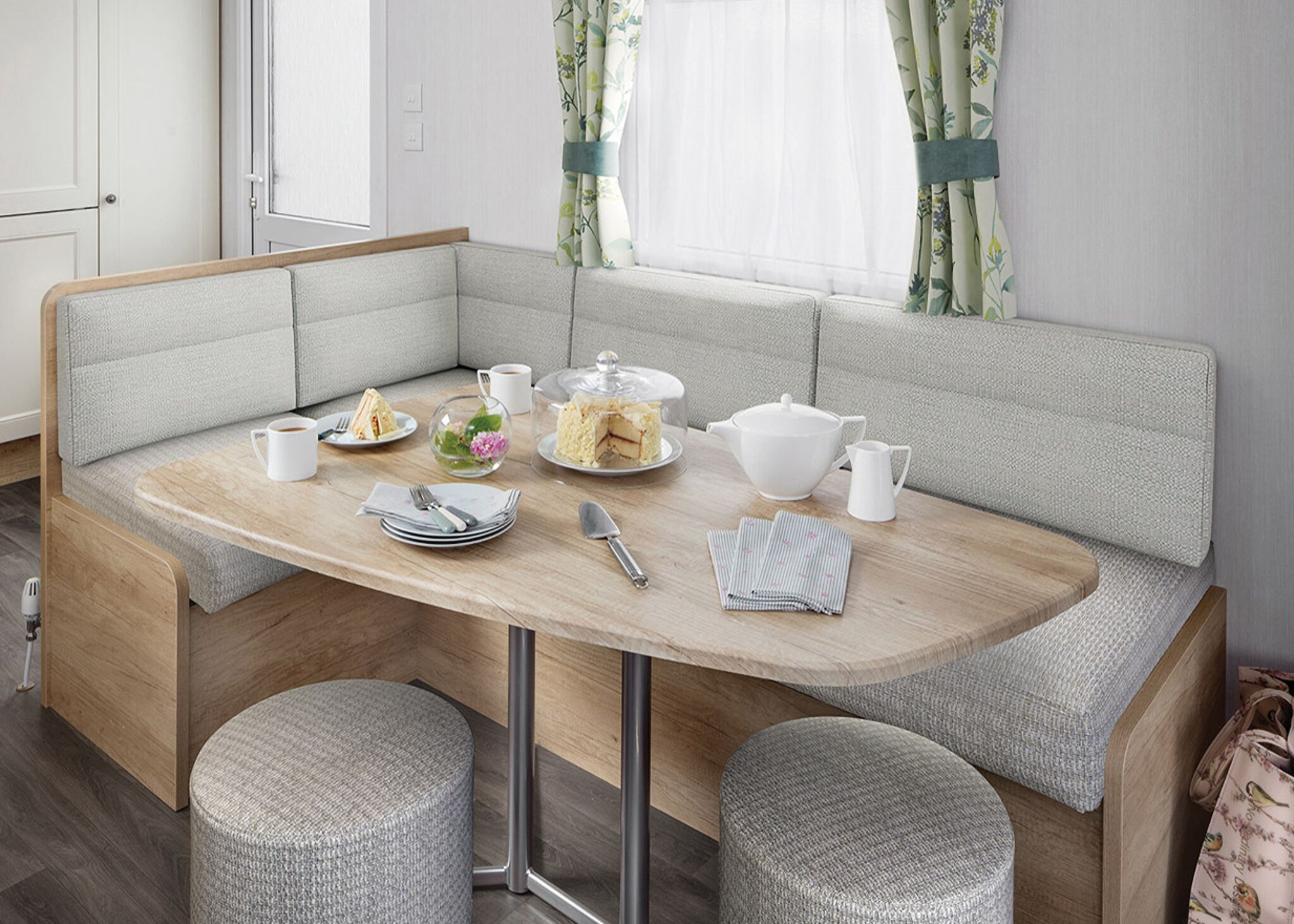 Une cuisine moderne et compacte, dotée d’un banc intégré avec des tabourets, d’une table à manger et d’une fenêtre agrémentée de rideaux.