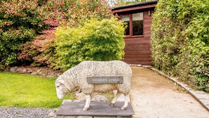 Eine Steinskulptur eines Schafs vor einem Holzgebäude, mit einem Schild, auf dem 'Vendee Lodge' steht.