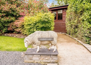 A stone sheep sculpture with a sign reading 'Vendee Lodge' in front of a wooden building. - Decadent lodge designed to exacting, luxury standards. (Cartmel)