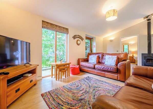 A living room with a TV, leather sofa, wooden coffee table, colorful rug, and a fireplace.