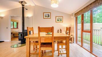 A dining area with a wooden table and chairs, a fireplace, and large windows with a view of greenery.
