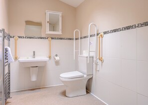 A small bathroom with a toilet, sink, and mirror. There are grab bars installed for safety. - Subtly decadent lodge designed to exacting, luxury standards. (Cartmel)