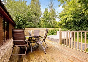 A wooden deck with a table and chairs, surrounded by a wooden fence and lush greenery. - Decadent lodge designed to exacting, luxury standards. (Cartmel)