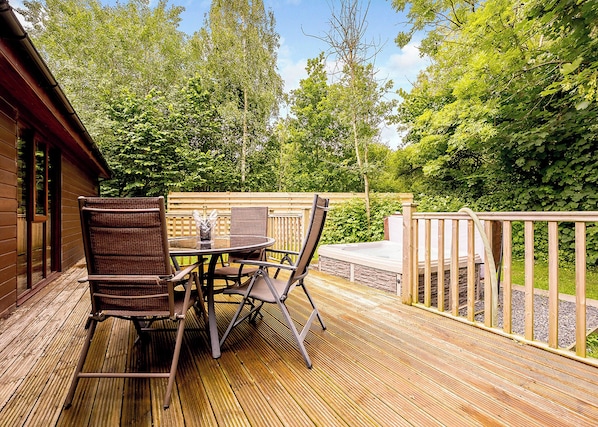 A wooden deck with a table and chairs, surrounded by a wooden fence and lush greenery. - Decadent lodge designed to exacting, luxury standards. (Cartmel)