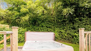 Ein Whirlpool in einem Garten mit Holzterrasse und Steinmauern.