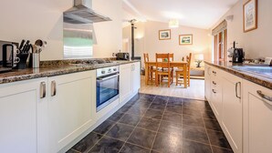 Eine moderne Küche mit weißen Schränken, einem Gasherd und einem eingebauten Backofen. Es gibt einen Essbereich mit einem Holztisch und Stühlen.