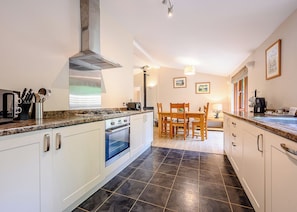 A modern kitchen with white cabinets, a gas stove, and a built-in oven. There is a dining area with a wooden table and chairs. - Decadent lodge designed to exacting, luxury standards. (Cartmel)