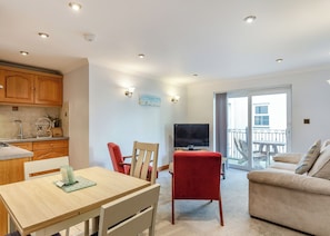 A modern kitchen with wooden cabinets, a dining area with a table and chairs, a TV, and a balcony with a view.