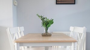 Une table à manger avec des chaises blanches, un vase avec des plantes vertes et un tableau encadré au mur.