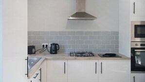 Une cuisine moderne avec des armoires blanches, une hotte en acier inoxydable, une cuisinière à gaz, une bouilloire et un four à micro-ondes.