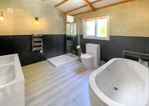 Um banheiro moderno com banheira, vaso sanitário, chuveiro e porta-toalhas.
