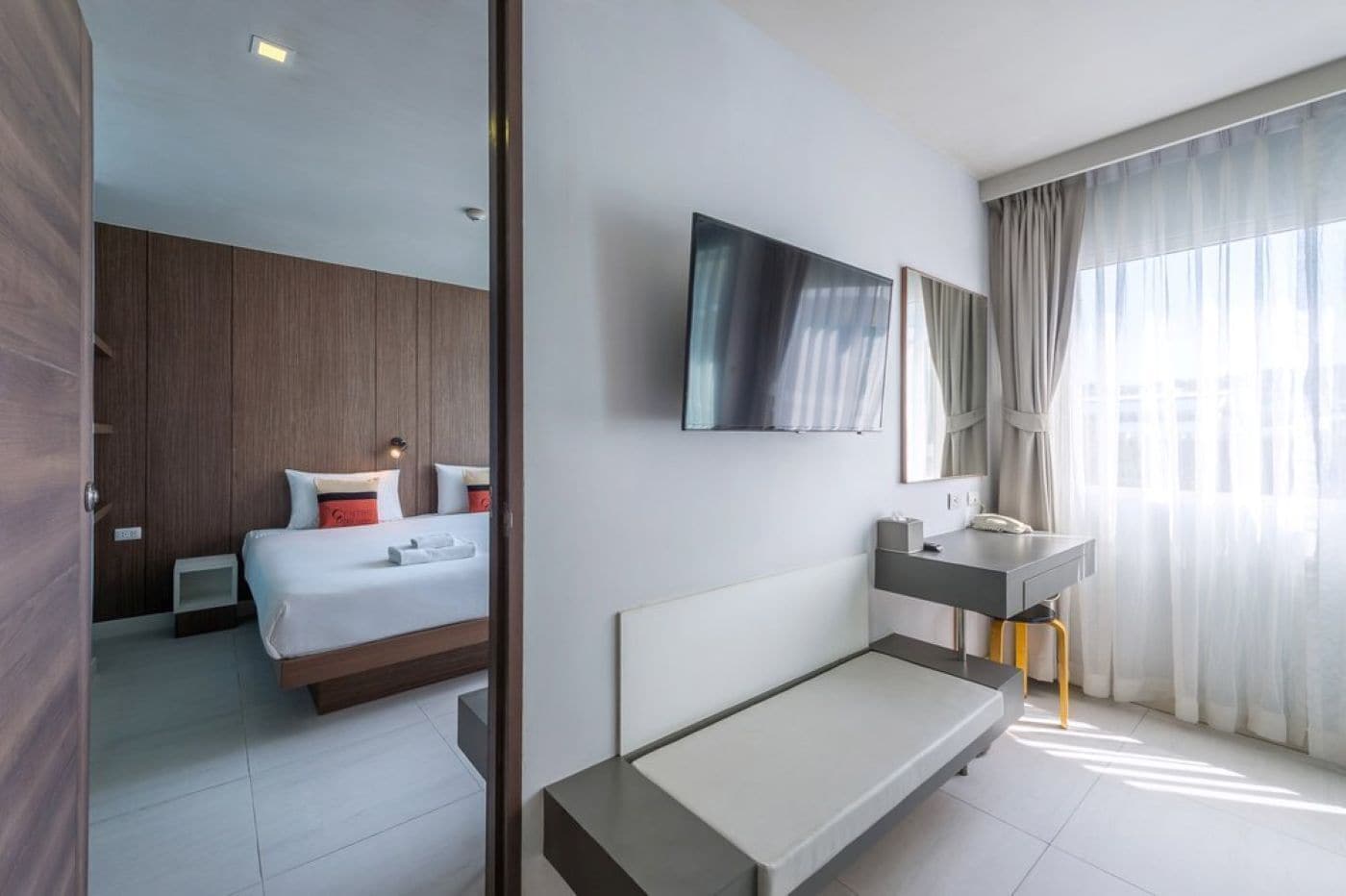 A modern hotel room with a bed, bedside table, and a large mirror.