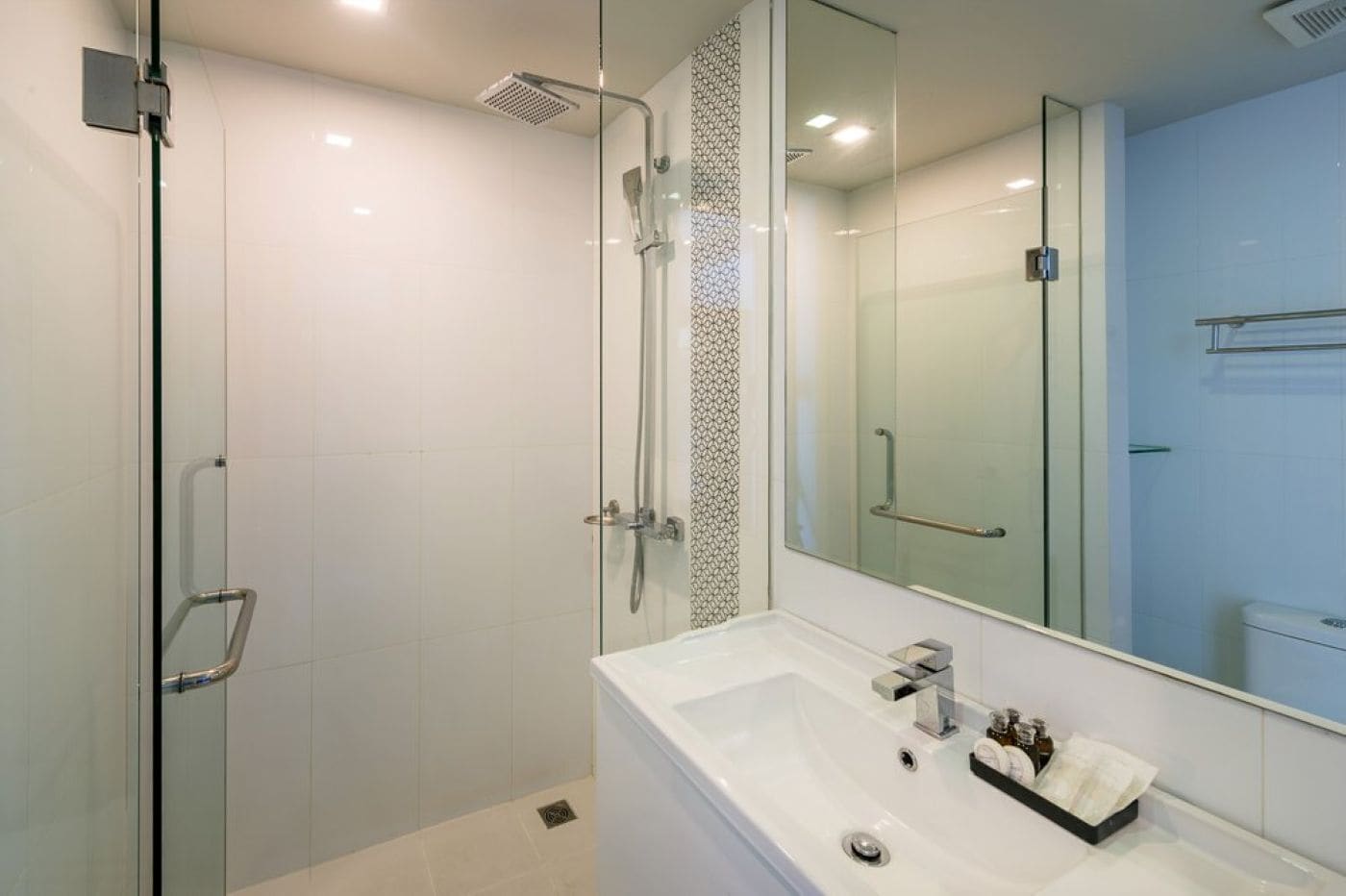A modern bathroom with a glass shower enclosure, a large mirror, and a white sink with toiletries.