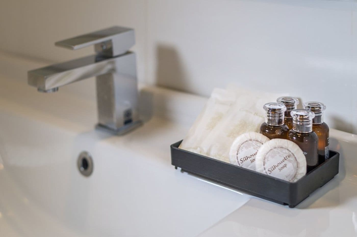 A bathroom sink with a modern faucet and a tray holding toiletries including bottles and a bar of soap.