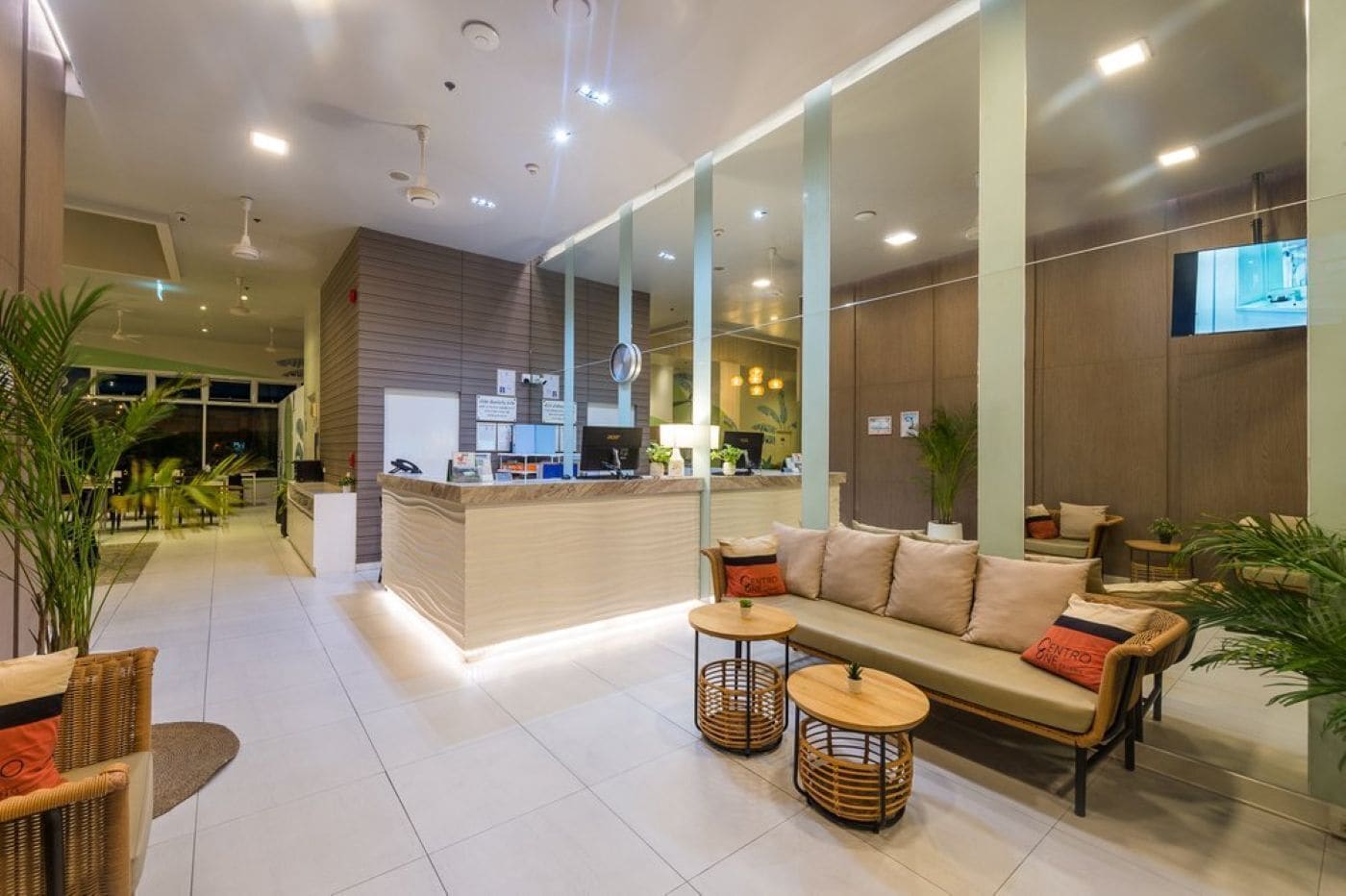 A modern hotel lobby with a reception desk, seating area, and a large mirror.