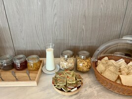 Un bufé de desayuno con frascos de conservas, una jarra de leche, cereales y pan.