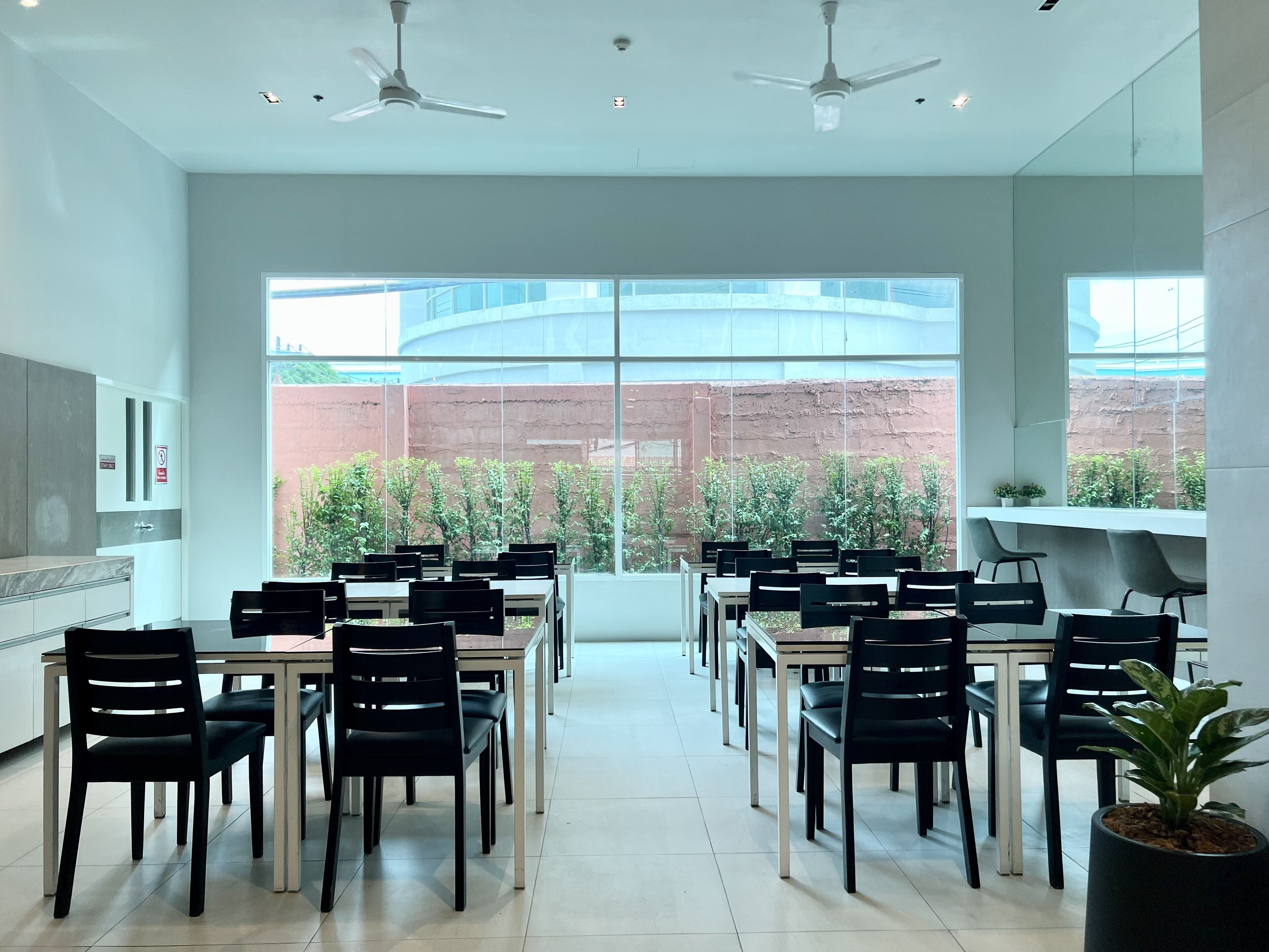 A modern dining area with tables and chairs, large windows, and ceiling fans.