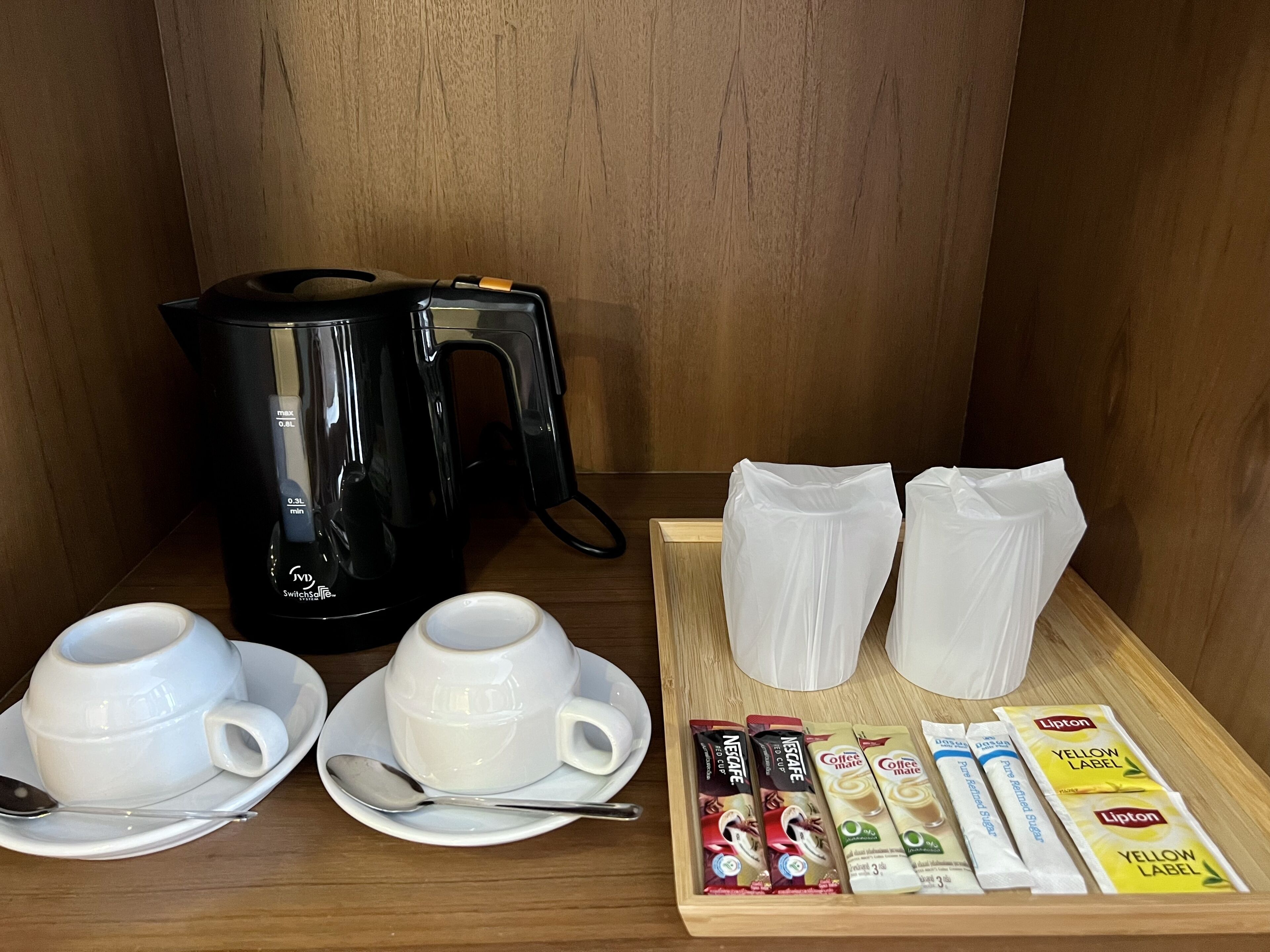 A coffee station with a black coffee maker, two white cups, two white mugs, a spoon, and several coffee pods.