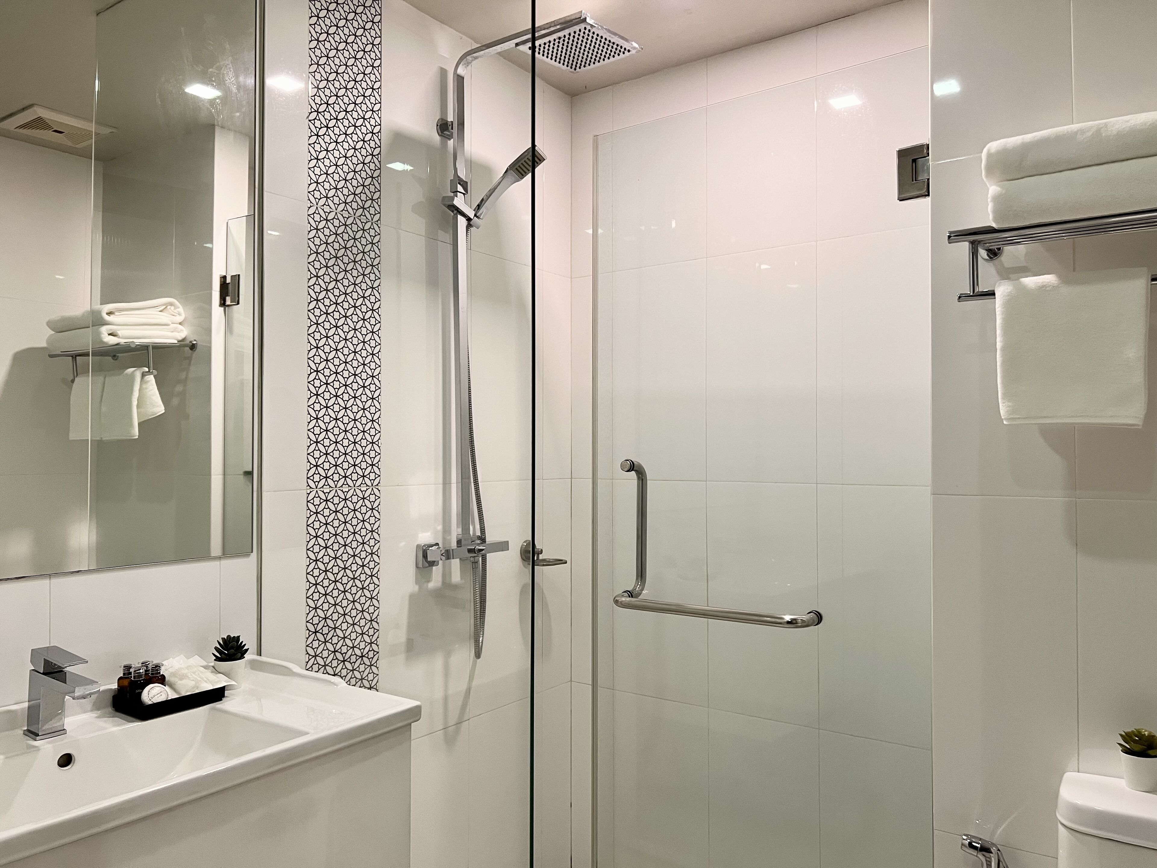 Ein modernes Badezimmer mit einer Duschkabine aus Glas, einem weißen Waschbecken mit Chromarmatur und einer Toilette mit Handtuchhalter.