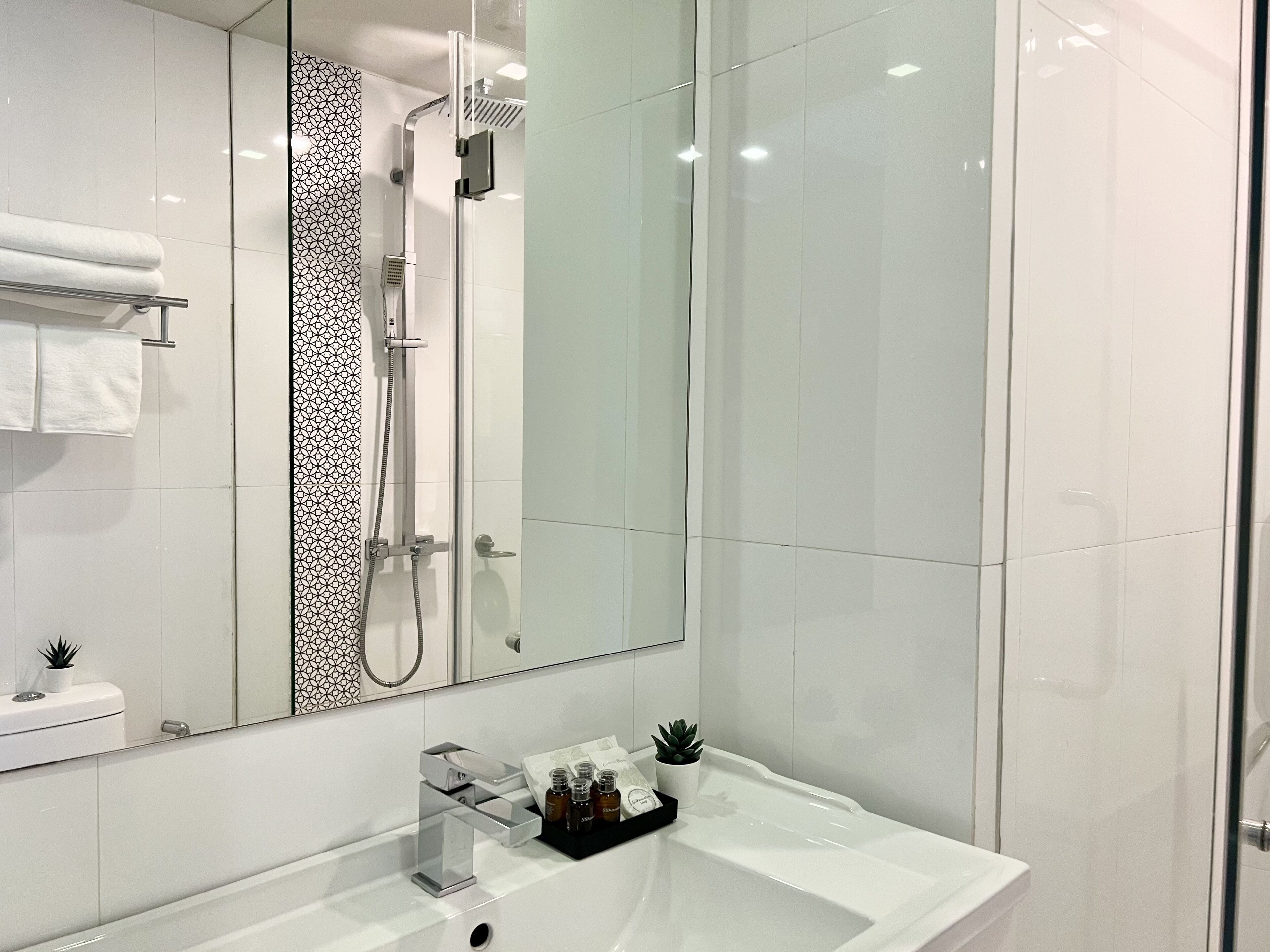 Une salle de bain moderne avec une douche à parois de verre, un grand miroir et un lavabo blanc agrémenté d’articles de toilette.