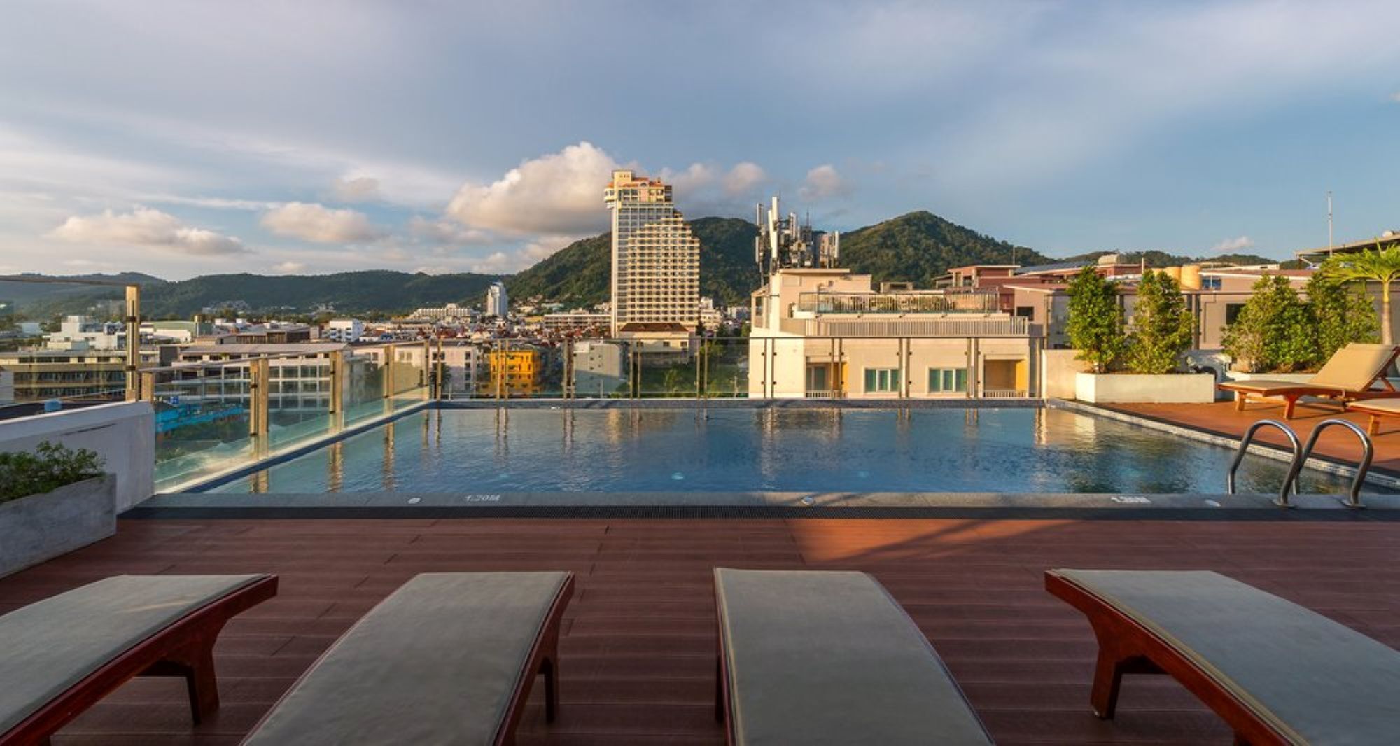A rooftop pool with lounge chairs, a clear view of a cityscape, and a mountain in the background.
