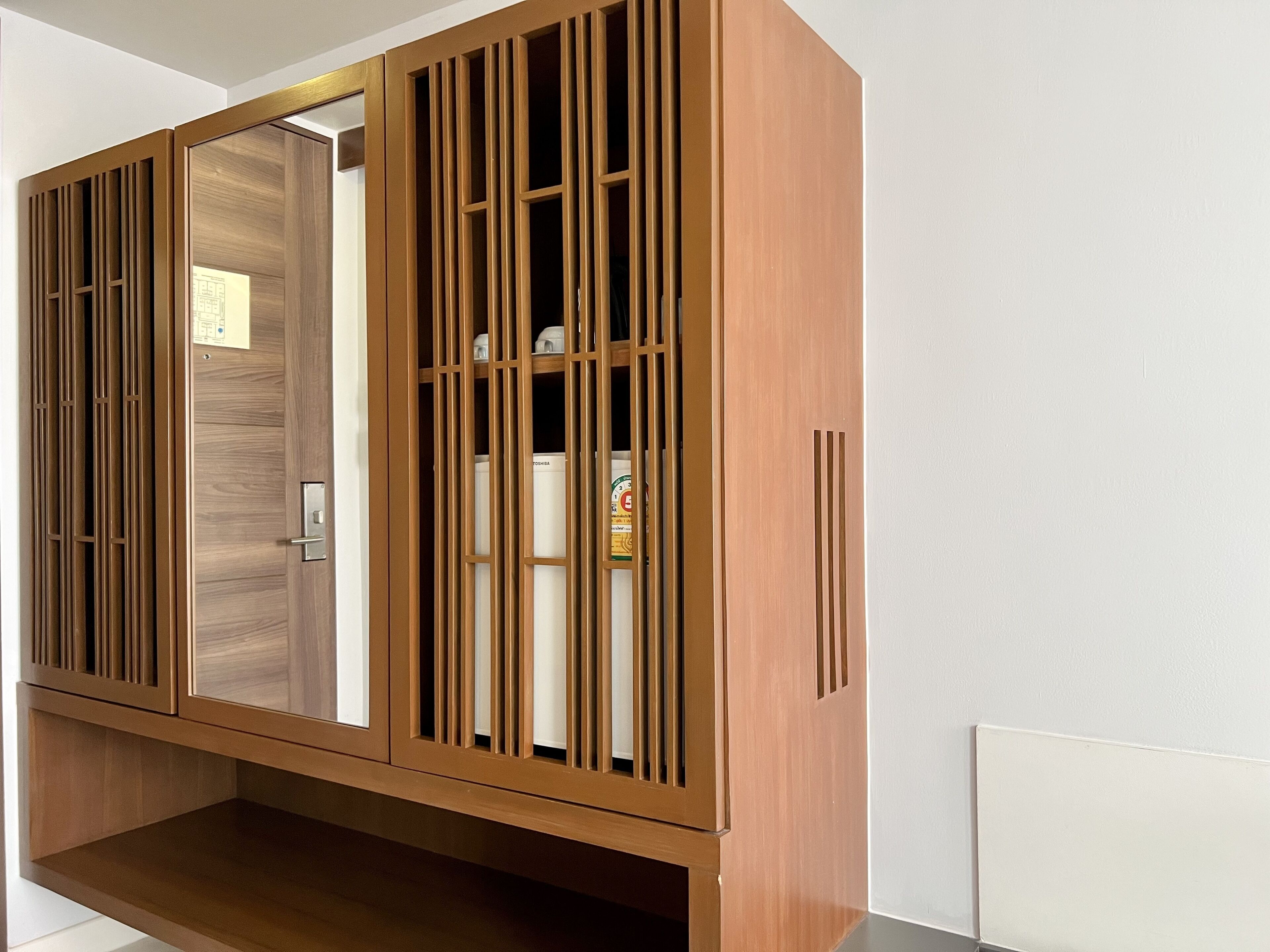 A wooden wardrobe with a mirrored door and vertical slats.
