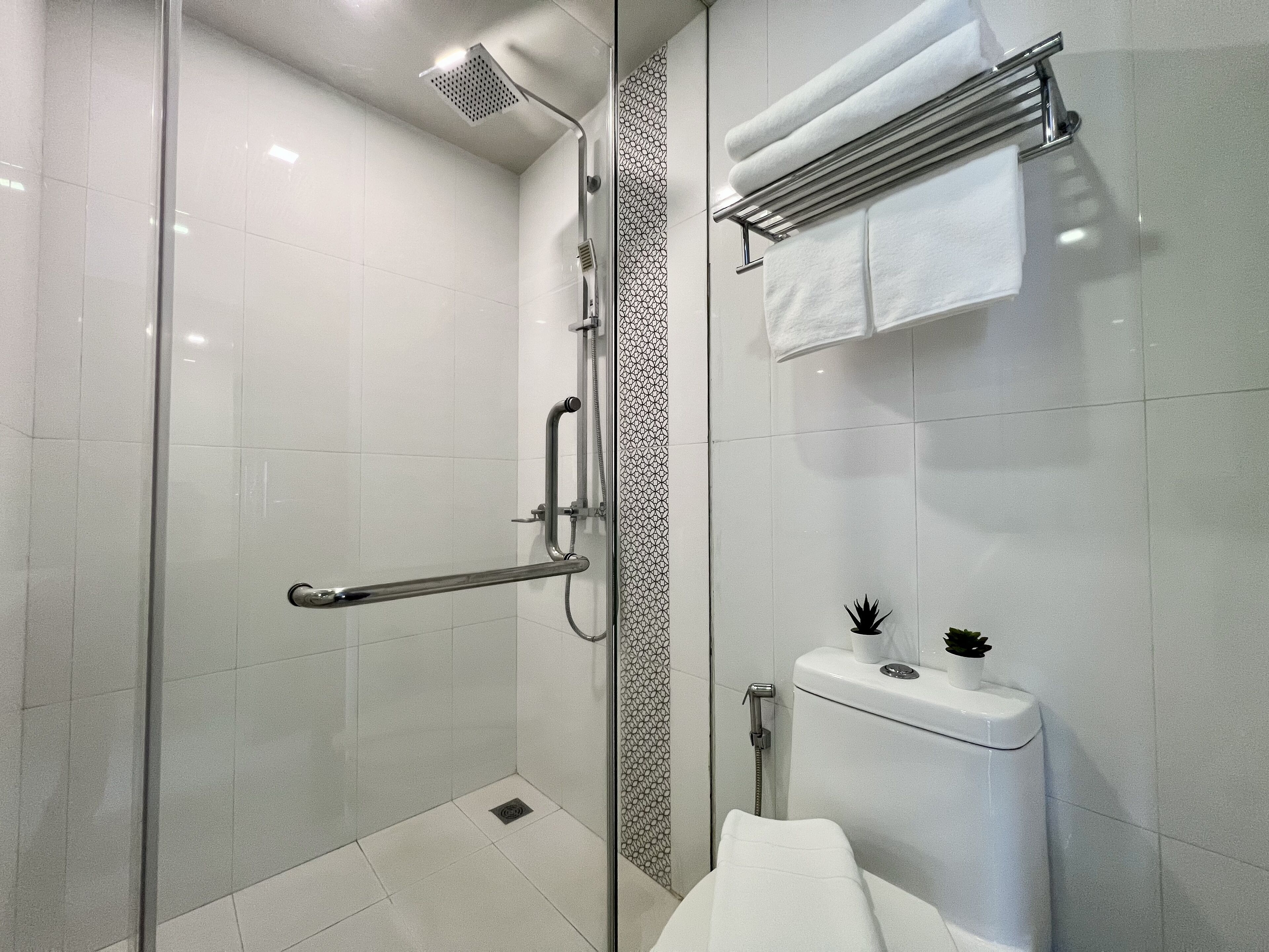 A modern bathroom with a glass-enclosed shower, a white toilet, and a towel rack with folded towels.
