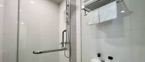 A modern bathroom with a glass-enclosed shower, a white toilet, and a towel rack with folded towels.