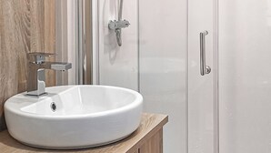 A bathroom with a white sink, a shower, and a wooden vanity.