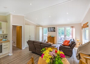 A spacious living area with a sofa, a dining table with flowers, a TV, and a balcony with outdoor furniture. - 2 bedroom accommodation in Cartmel (Cartmel)