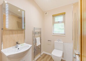 A bathroom with a sink, mirror, towel rack, toilet, and window with blinds.