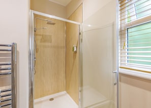 A bathroom with a shower, a toilet, and a window with blinds.