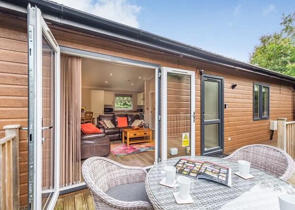 Un chalet confortable doté d’une porte-fenêtre coulissante qui donne sur un espace de vie, d’une table à manger avec deux chaises et d’un fauteuil en osier à l’extérieur.