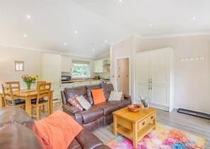 A modern living room with a leather sofa, wooden coffee table, and a dining area with a table and chairs. - 1 bedroom accommodation in Cartmel (Cartmel)