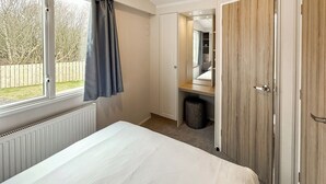 Ein Schlafzimmer mit Bett, einem Fenster mit Vorhängen, einem Kleiderschrank und einem Spiegel.