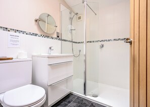 A bathroom with a toilet, sink, mirror, and glass-enclosed shower.