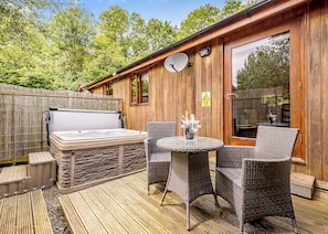 A wooden outdoor deck with a hot tub, wicker chairs, and a table.