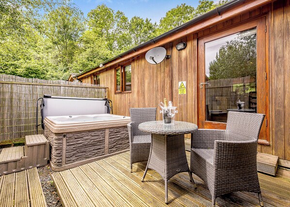 A wooden outdoor deck with a hot tub, wicker chairs, and a table.