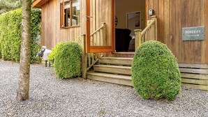 Un bâtiment en bois avec un escalier en bois menant à une porte, une enseigne indiquant « BORERAY », et un petit jardin agrémenté d’arbustes taillés.