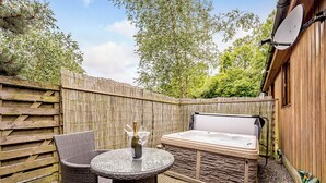 Un espace extérieur aménagé avec un jacuzzi, des meubles en osier et une clôture en bois.