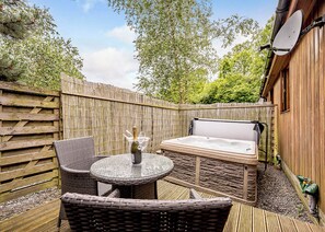 Un espace extérieur aménagé avec un jacuzzi, des meubles en osier et une clôture en bois.