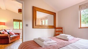 Une chambre à coucher avec un lit, une chaise en bois, un canapé en cuir marron, un grand miroir et une fenêtre.
