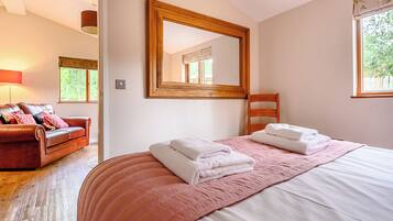 A bedroom with a bed, a wooden chair, a brown leather sofa, a large mirror, and a window.