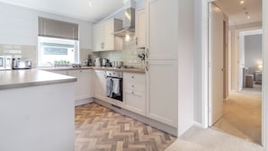 Una cocina moderna con armarios blancos, suelo de madera en espiga y horno visible.